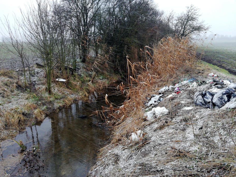 Hromada odpadků na břehu potoka.
